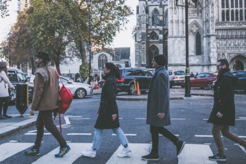 4 people crossing the street one after the other like the Beatles next to Westminster Abbey