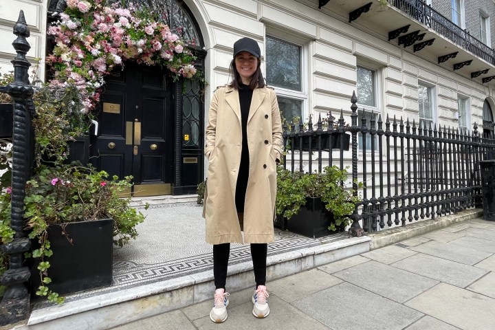 Person in coat and cap stands in front of a flower-adorned building entrance.